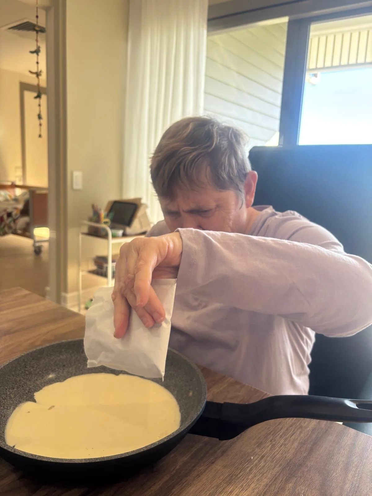 A participant pouring pancake batter into a pan in their own kitchen